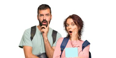 Sırt çantaları ve kitapları olan iki öğrenci, izole edilmiş beyaz arka plana bakarken şaşırıp şok edeşer