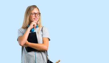 Gözlüklü öğrenci kız ayakta ve mavi arka plan üzerinde çene üzerinde el ile yan bakıyor