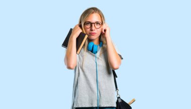 İki kulağını da elleriyle kaplayan gözlüklü öğrenci kız. Mavi arka planda sinirli ifade