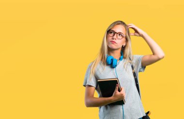 Sarı arka plan üzerinde başını çizerken gözlüklü ve kafa tetkiklerini karıştıran öğrenci kız