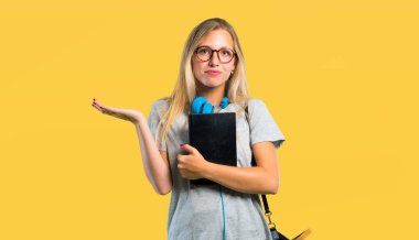 Sarı arka planda elleri ve omuzları kaldırırken gözlüklü ve yüz ifadesini karıştıran öğrenci kız