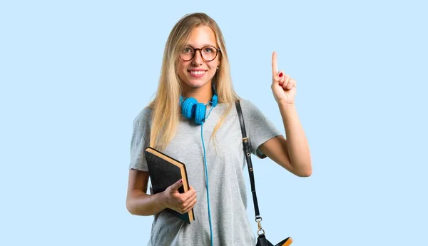 Student girl with glasses showing and lifting a finger in sign of the best on blue background