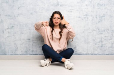 Bir masada okuyan genç öğrenci kız iyi-kötü işareti yapıyor. Evet ya da değil arasında kararsız