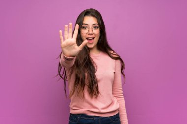 Teenager girl over purple wall counting five with fingers clipart