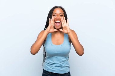 Izole mavi arka plan üzerinde uzun örgülü saçlı Afro-Amerikan genç kız ağız geniş açık bağırarak