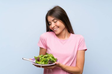 Izole mavi arka plan üzerinde salata ile genç kadın