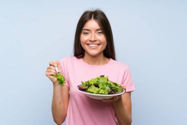 Izole mavi arka plan üzerinde salata ile genç kadın