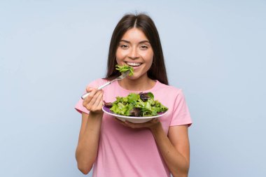 Izole mavi arka plan üzerinde salata ile genç kadın