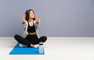 Genç spor kadın mat gülümseyerek katta oturan ve zafer işareti gösteren