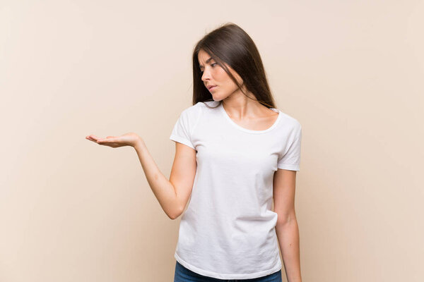 Pretty young girl over isolated background holding copyspace with doubts