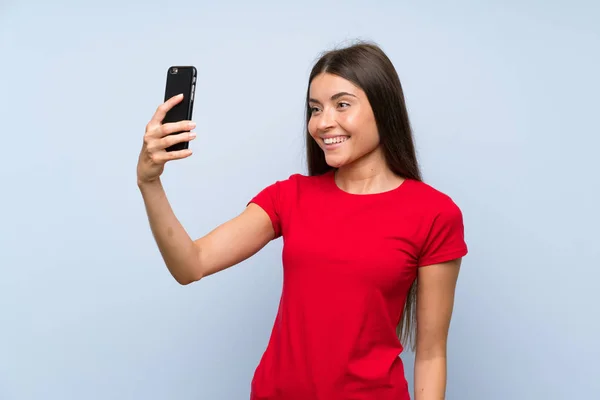 İzole mavi duvar üzerinde selfie yapma cep telefonu ile Esmer genç kadın — Stok fotoğraf