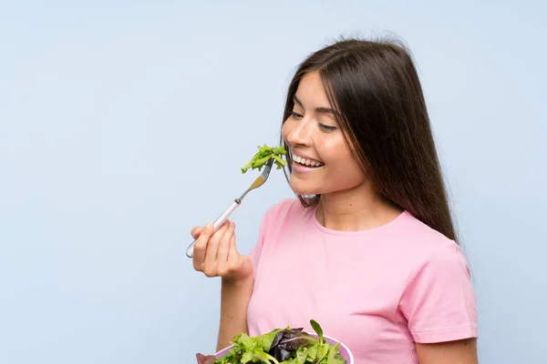 Young woman with salad over isolated blue background