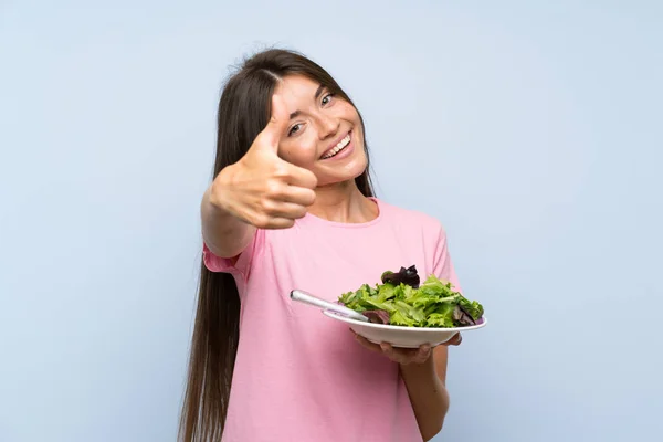 年轻女子与沙拉孤立的蓝色背景竖起大拇指 因为发生了一些好事 — 图库照片