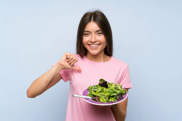 Young woman with salad over isolated blue background proud and self-satisfied