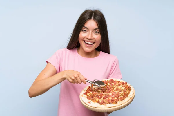Linda joven sosteniendo una pizza sobre una pared azul aislada — Foto de Stock