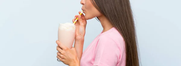 Jovem com batido de morango sobre fundo azul isolado — Fotografia de Stock