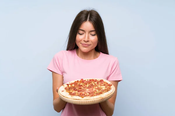 Linda joven sosteniendo una pizza sobre una pared azul aislada — Foto de Stock