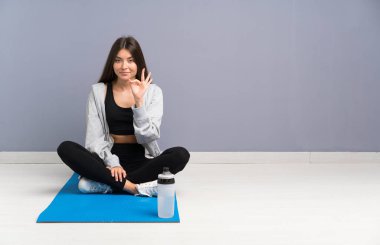 Genç spor kadın parmakları ile ok işareti gösteren mat ile katta oturan