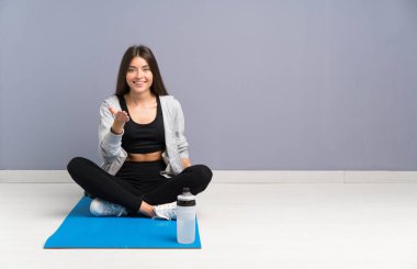 Young sport woman sitting on the floor with mat handshaking after good deal