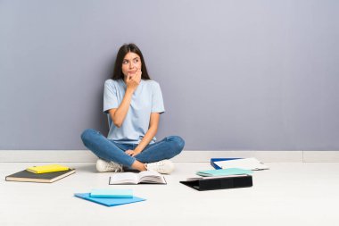 Yerde birçok kitap ile genç öğrenci kadın bir fikir düşünme