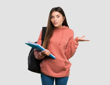 Dizüstü bilgisayar tutan genç öğrenci kadın izole gri arka plan üzerinde şüphe jest yapıyor