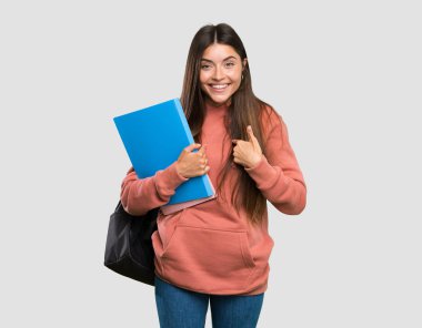 İzole gri arka plan üzerinde sürpriz yüz ifadesi ile defter tutan genç öğrenci kadın