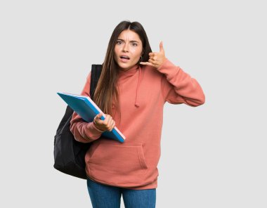 Genç öğrenci kadın telefon hareketi yapma defterleri tutan ve izole gri arka plan üzerinde şüphe