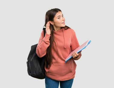 İzole gri arka plan üzerinde kulağına el koyarak bir şey dinleyerek dizüstü tutan genç öğrenci kadın