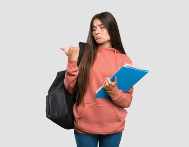 Genç öğrenci kadın mutsuz deftertutan ve izole gri arka plan üzerinde yan işaret