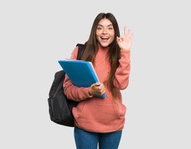 Genç öğrenci kadın dizüstü bilgisayarlar tutan şaşırttı ve izole gri arka plan üzerinde ok işareti gösteren