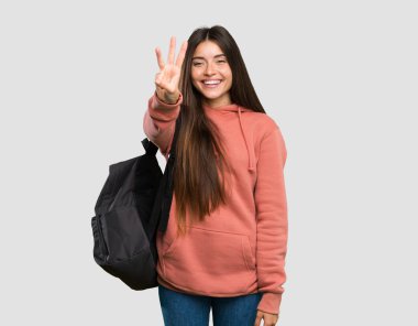 Genç öğrenci kadın defterleri mutlu tutan ve izole gri arka plan üzerinde parmakları ile üç sayma