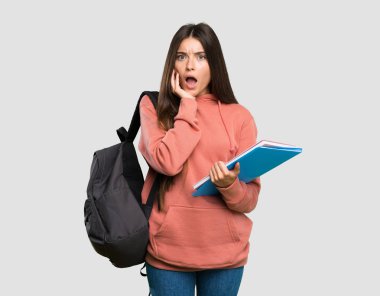 Tecrit edilmiş gri arka plana bakarken defter tutan genç öğrenci kadın şaşırmış ve şok emiş