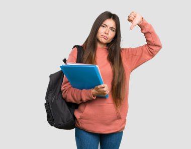 İzole gri arka plan üzerinde başparmak gösteren deftertutan genç öğrenci kadın