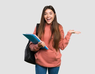 İzole gri arka plan üzerinde şok yüz ifadesi ile dizüstü tutan genç öğrenci kadın