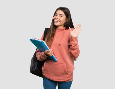 Genç öğrenci kadın izole gri arka plan üzerinde mutlu ifade ile el ile selamlama defterleri tutan