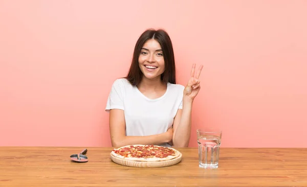 Young woman with a pizza smiling and showing victory sign