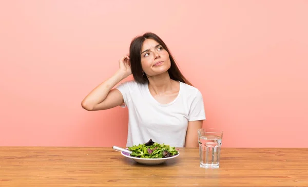 Young woman with a salad having doubts and with confuse face expression