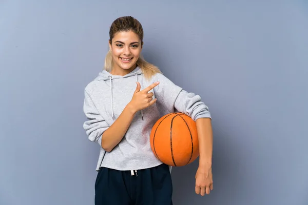 製品を提示するために側面を指し 灰色の壁の上にバスケットボールをしているティーンエイジャーの女の子 — ストック写真