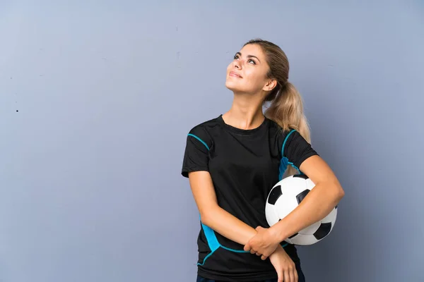 笑顔で見上げる灰色の壁の上にブロンドサッカー選手ティーンエイジャーの女の子 — ストック写真