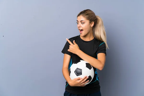 Rubia Futbolista Adolescente Chica Sobre Gris Pared Sorprendida Apuntando Lado —  Fotos de Stock