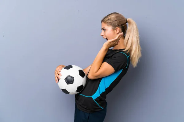 驚きの表情で灰色の壁の上にブロンドサッカー選手ティーンエイジャーの女の子 — ストック写真