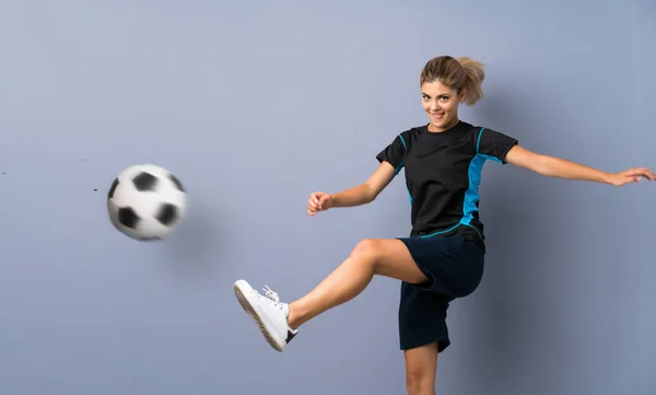 灰色の壁の上にブロンドサッカー選手ティーンエイジャーの女の子 — ストック写真