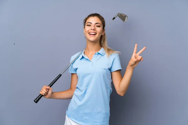 青少年高尔夫球手女孩在灰色的墙壁微笑 并显示胜利标志 — 图库照片