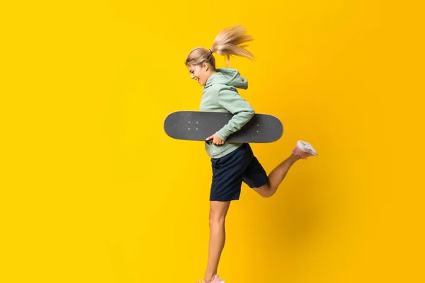ブロンドティーンエイジャースケーターの女の子は孤立した黄色の背景を飛び越える — ストック写真