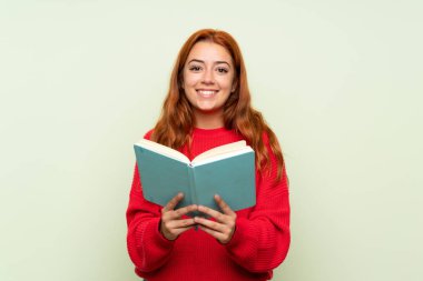 Izole yeşil arka plan üzerinde kazak ile Genç redhead kız tutma ve bir kitap okuma