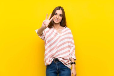 Soyutlanmış sarı arka plan mutlu ve parmaklarıyla üçe kadar sayıyor.