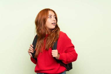 Sırt çantası ile izole yeşil arka plan üzerinde kazak ile Genç redhead kız