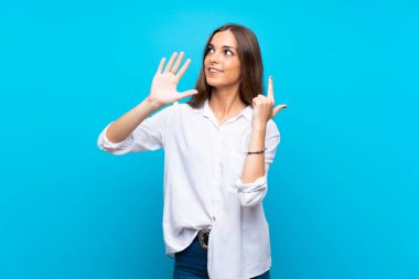 İzole edilmiş mavi arka plan üzerinde genç bir kadın parmaklarıyla yediyi sayıyor