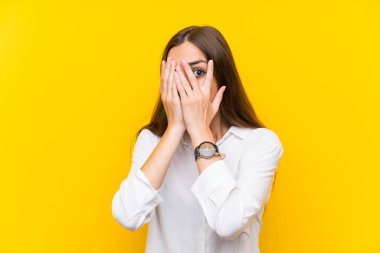 Gözleri kaplayan ve parmaklardan bakan izole sarı arka plan üzerinde genç kadın