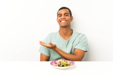 Bir masada salata ile genç yakışıklı adam gelmeye davet için yan ellerini uzatıyor